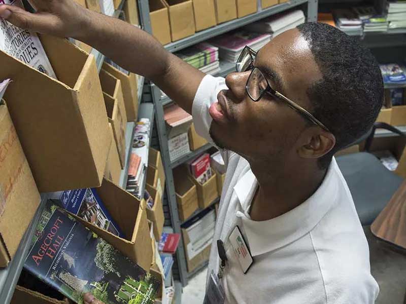 a student looking through a box of books in a room full of boxed books